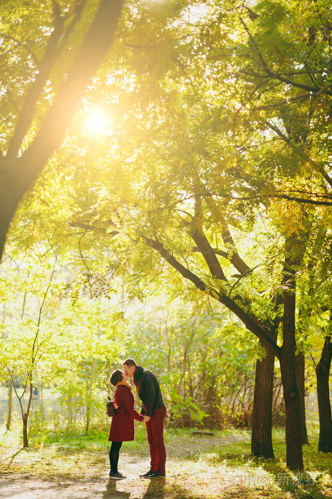 年轻热情的情侣在阳光明媚的天气里在秋天的城市公园里带着背包的男人