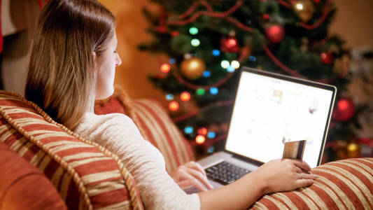 在圣诞前夕坐在扶手椅上的年轻女子, 并作出网上购买