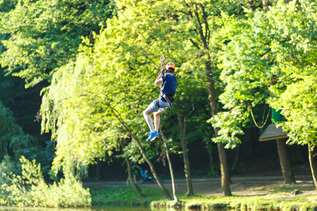 快乐可爱的小男孩穿着蓝色T恤和头盔，在冒险公园玩，拿着绳子和爬木楼梯。 积极的生活方式概念