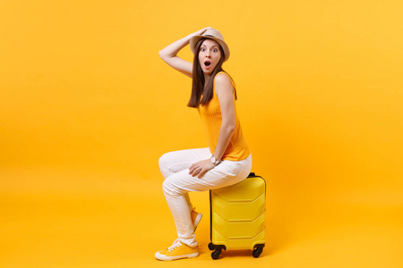 旅行者旅游妇女戴着夏季休闲服装帽，坐在黄色橙色背景下的手提箱上。 女乘客在周末出国旅行，度假。 航空飞行旅程概念