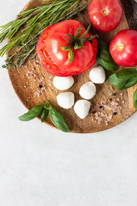 莫扎雷拉和番茄与罗勒叶，迷迭香和百里香在木盘上。 意大利沙拉酱的原料。 复制空间