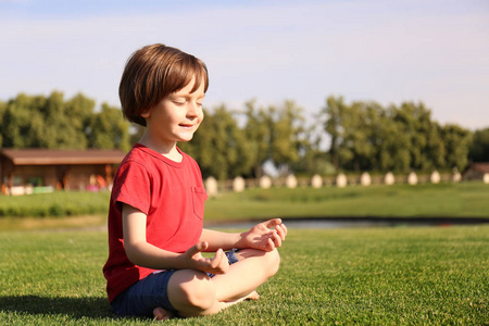 阳光明媚的一天，可爱的小男孩在公园里练习瑜伽