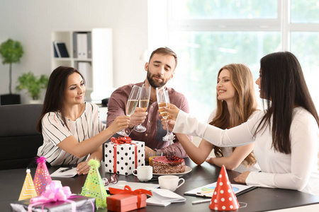 在办公室的生日聚会上，年轻的同事们拿着香槟碰杯