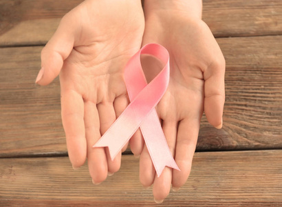 女人在木制背景上拿着粉红色的丝带。乳腺癌认识概念