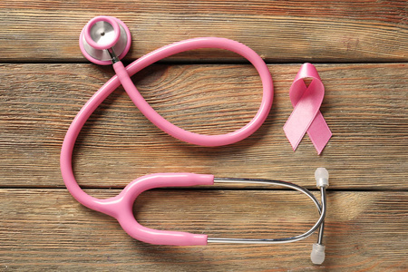 木制背景上的粉红色丝带和听诊器。乳腺癌认识概念