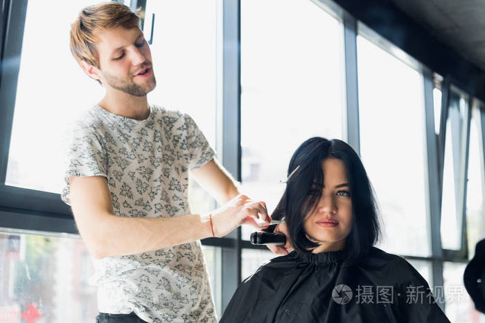 快关门女理发师在美容院用熨斗把棕色头发理直女造型师在美发厅为年轻
