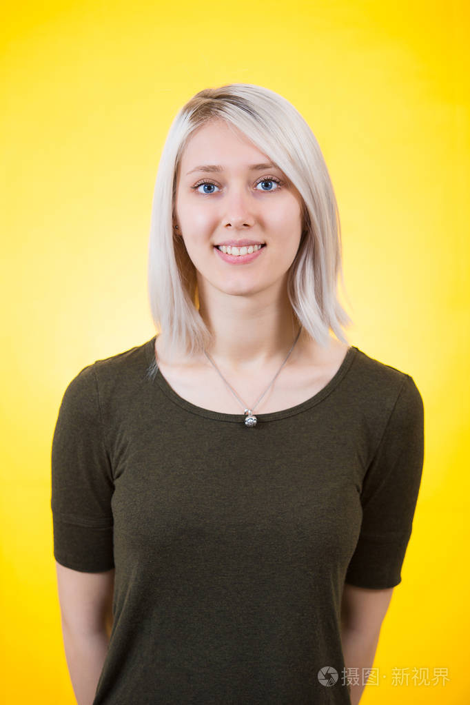 开朗的年轻女人看着相机,双手背在背后,被黄色的五颜六色的背景隔离.