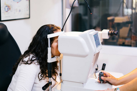 眼科医生在检查室里，年轻女子坐在椅子上看着眼科试验机