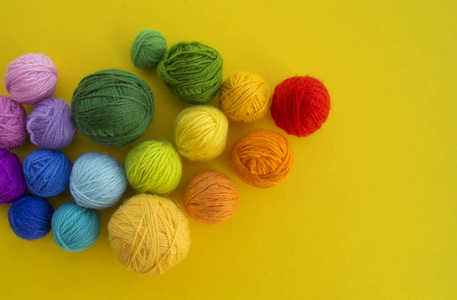 在黄色背景上编织彩虹颜色的很多球。 最喜欢的爱好。 编织帽子的过程。