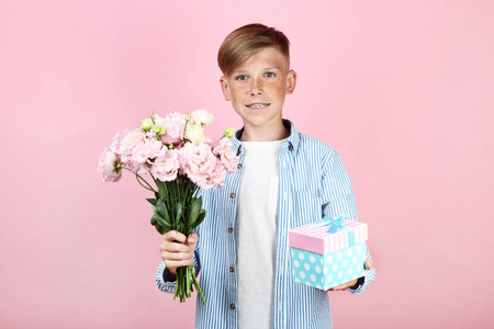 漂亮的小男孩，有粉红色背景的鲜花和礼品盒