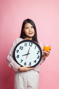 带钟的亚洲女人在粉红色背景下喝橙汁