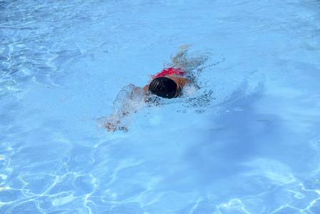 白种人在阳光明媚的日子里在室外游泳池里自由泳。 那个人穿着红色泳衣和黑色帽子。 休闲时游泳