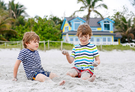 两个小朋友玩得很开心, 在热带海滩上建造沙子城堡, 快乐最好的朋友玩耍。兄弟姐妹, 双胞胎与棕榈和家庭背景。洛杉矶的家庭生活