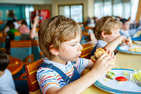 可爱健康的学龄前孩子男孩吃汉堡包坐在学校或幼儿园的咖啡馆。快乐的孩子在餐馆里吃健康的有机和素食食物。童年，健康概念