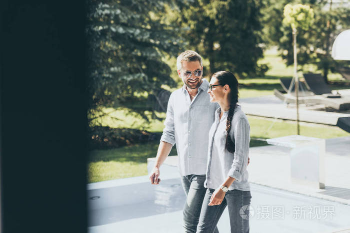 微笑的夫妇戴着太阳镜在乡间别墅散步