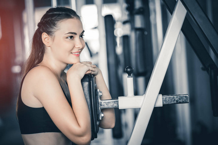 适合漂亮的年轻女人在健身房的机器上锻炼。 高兴的微笑女孩喜欢她的训练过程。 健身理念健康运动生活方式