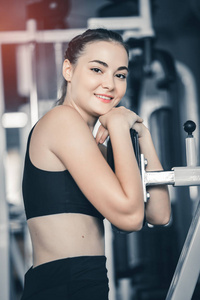 适合漂亮的年轻女人在健身房的机器上锻炼。 高兴的微笑女孩喜欢她的训练过程。 健身理念健康运动生活方式