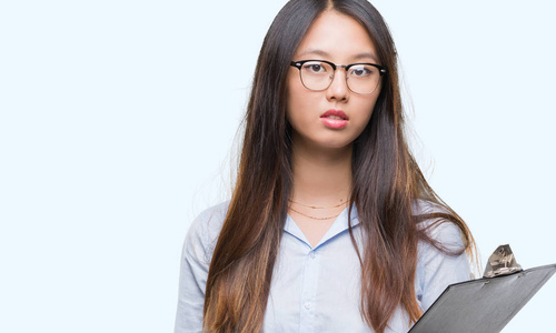 年轻的亚洲商界女性在孤立的背景下拿着剪贴板，聪明的脸上有自信的表情，认真的思考