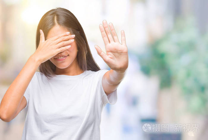 年轻的亚洲女人在孤立的背景上用手遮住眼睛,用悲伤和恐惧的表情做