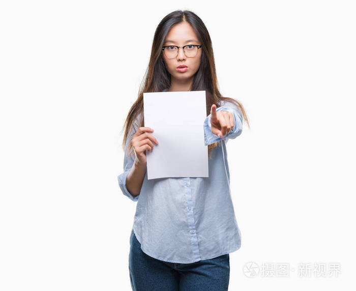 年轻的亚洲女人拿着白纸在孤立的背景上,手指着相机,向你手势正面和