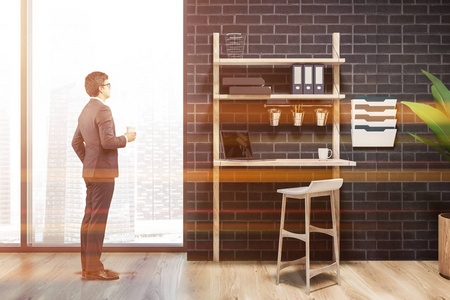 穿着极简主义自由职业者工作场所内部的人，有一个阁楼的窗户，黑色的砖墙，一个木制的地板和一张带凳子和笔记本电脑的桌子。三维渲染模拟