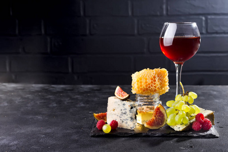 葡萄, 奶酪, 无花果和蜂蜜在石头黑色背景的红色的玻璃, 复制空间