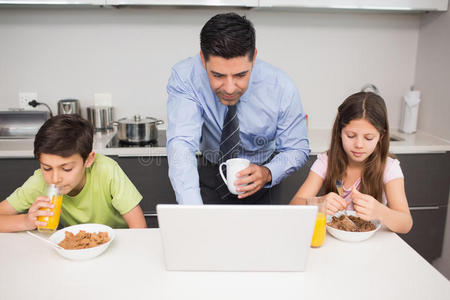 父亲用笔记本电脑和孩子在厨房吃早餐
