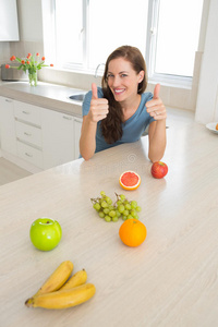 一个微笑的女人在厨房里竖起大拇指拿着水果