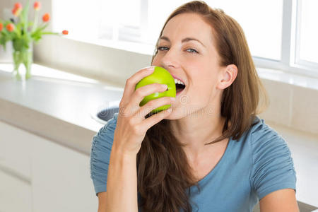 微笑的年轻女子在厨房吃苹果