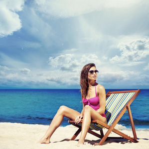 穿着泳衣的年轻女子在海滩上的躺椅上放松