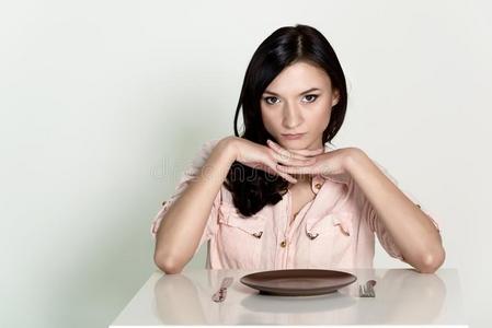美丽的黑发女人坐在一个空盘子里等待她的午餐