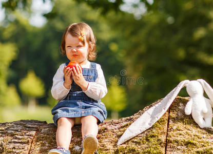 在夏日公园吃新鲜苹果的小女婴。