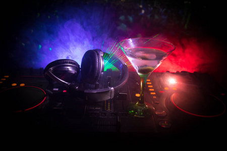 玻璃与马提尼与橄榄在DJ控制器在夜总会。 DJ控制台与俱乐部饮料在夜总会的音乐派对与迪斯科灯。