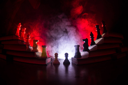 商业层次。 策略概念与棋子。 国际象棋站在书的金字塔上，国王在顶端。 暗雾背景与色调的光。 复制空间。