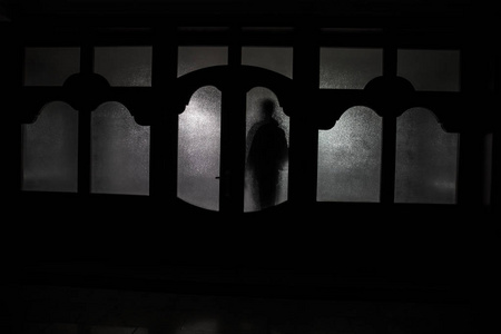 夜晚在窗户前的人类的轮廓. 可怕的场景万圣节概念模糊剪影的疯子.