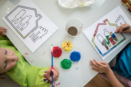两个孩子在房子里画一个家庭的素描，上面有五颜六色的丙烯酸颜料。