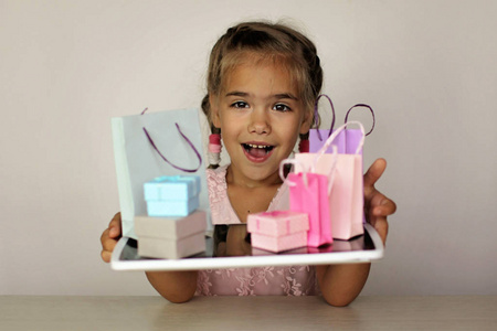 可爱的小学龄前女孩拿着一个平板电脑，上面有很多不同颜色的购物袋。网络购物，销售，礼品，节假日..美容和时尚概念