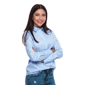 一位身穿蓝色衬衫和牛仔裤，双臂交叉在白色背景上微笑的黑发女人的肖像。