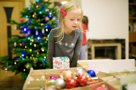 可爱的小女孩用五颜六色的玻璃包装饰圣诞树。 修剪圣诞树。 在家里庆祝圣诞节。