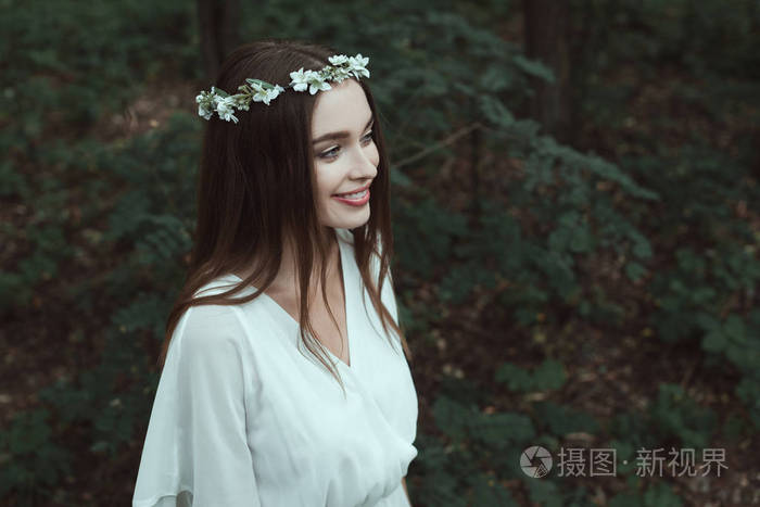 穿着白色连衣裙和花圈在树林里的时髦微笑女孩