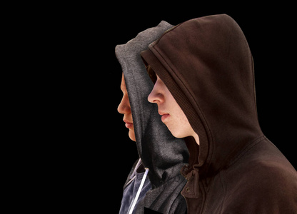 两个穿着黑色连帽衫的十几岁的男孩站在旁边，被孤立在黑色背景上