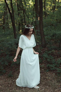 穿着白色连衣裙在森林里散步的美丽温柔的女孩