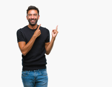 成年西班牙裔男子在孤立的背景上微笑，看着相机，用两只手和手指指向一边。