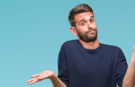 年轻的帅哥穿着冬天的毛衣,在孤立的背景上毫无头绪,表情混乱,举起