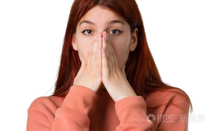 年轻的红头发女孩穿着粉红色的运动衫用双手捂住嘴因为她说了一些不