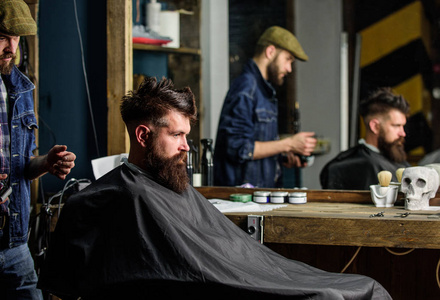 理发师准备理发剪胡子的人, 理发店背景。时髦的客户覆盖了海角得到理发。理发师和无情的大胡子客户。时髦的生活方式概念