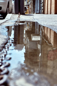夏天下雨后，城市街道和建筑物在路面不平的沥青水坑中被撕裂