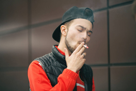 香烟关门秋天,一个年轻英俊的戴着黑色帽子的白胡子男人在街上抽烟.