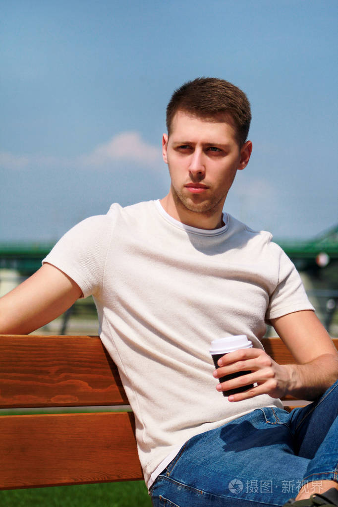 帅哥坐在码头上的长凳上喝咖啡去. 从城市高峰休息一下.