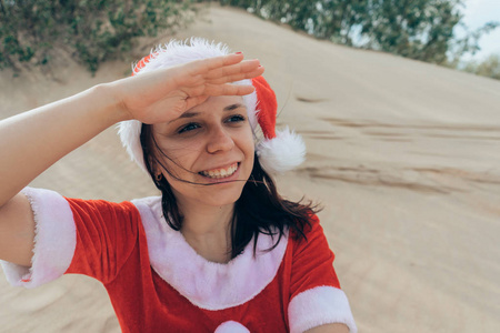 一个在沙漠里打扮成圣诞老人的女孩。 新年假期旅行的概念。 新年快乐，圣诞快乐